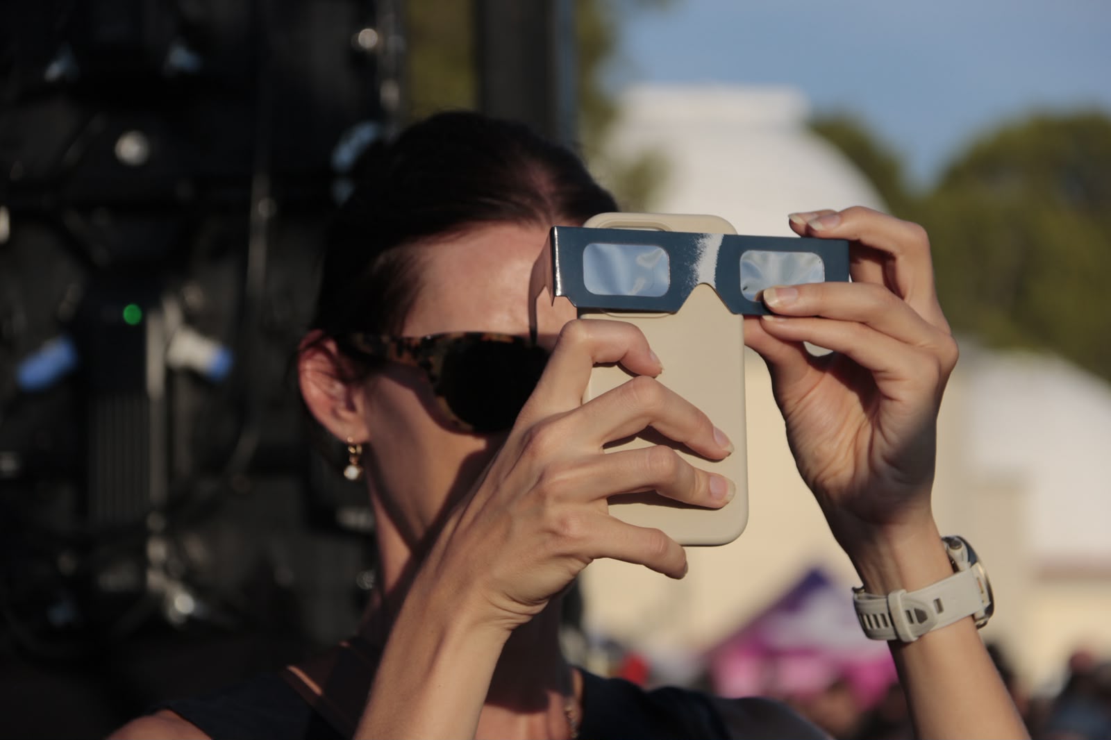 A woman puts eclipse glasses over her phone at the Ebre Observatory in Roquetes