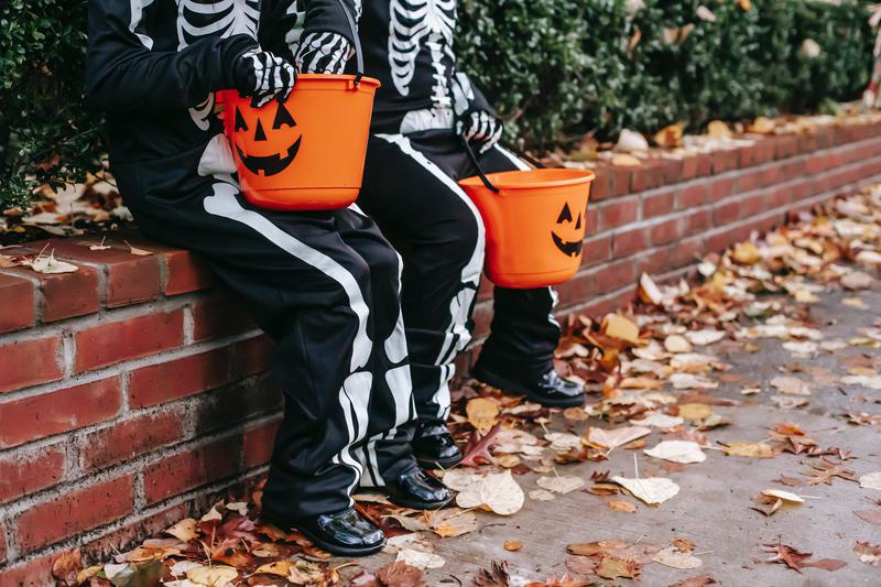 Children in Halloween costumes resting on a fence with jack-o-lantern buckets on October 30, 2020