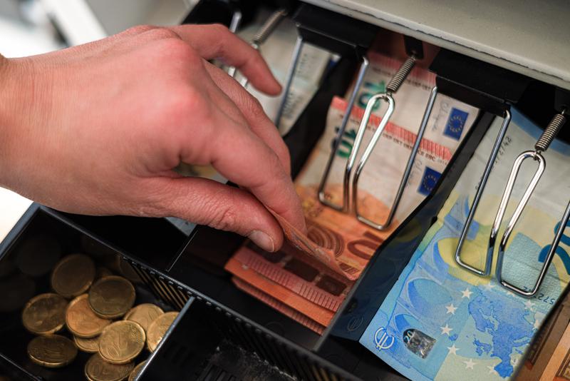 A hand holds bills and coins in a box