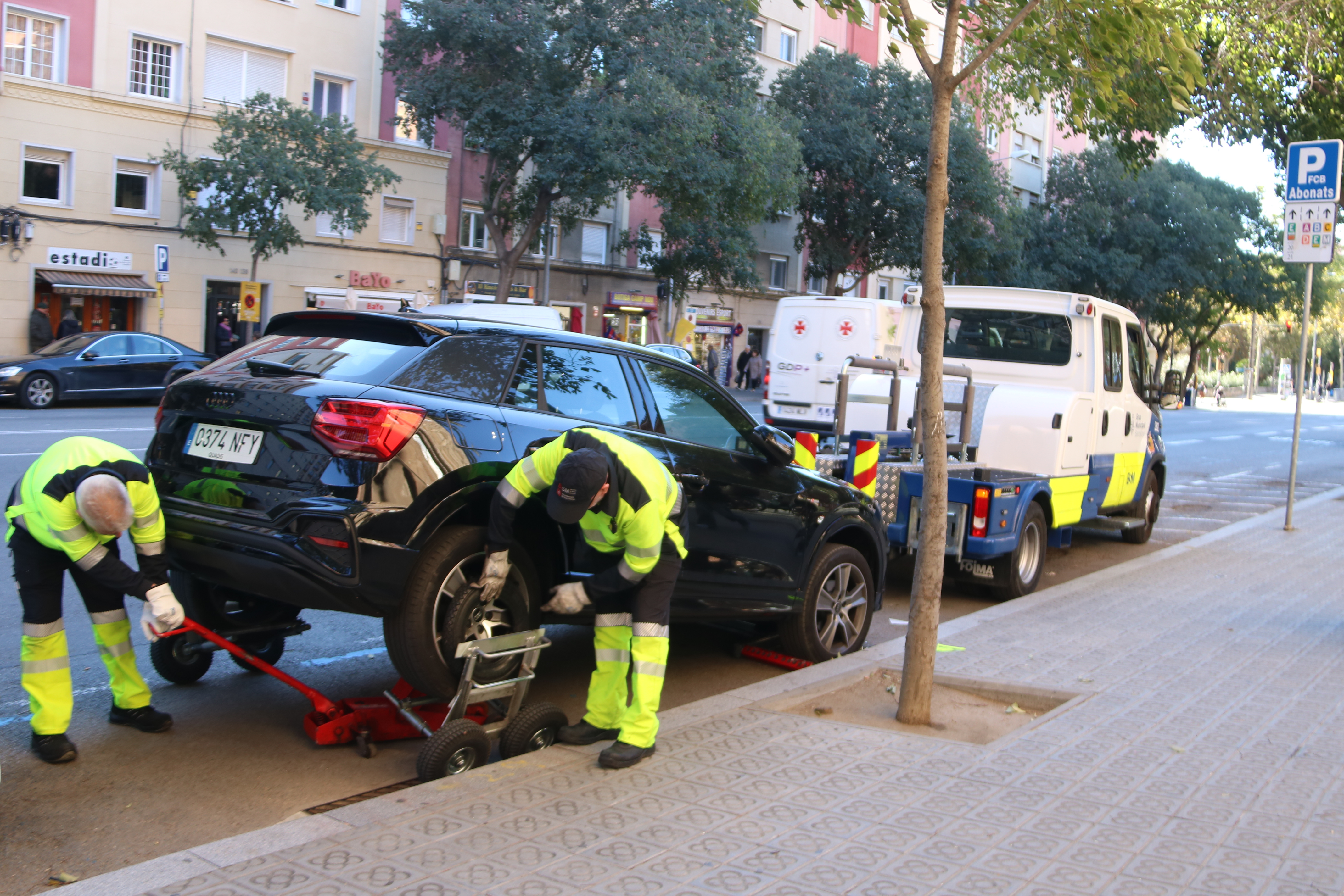 Two workers move a car from a no-parking zone next to Spotify Camp Nou