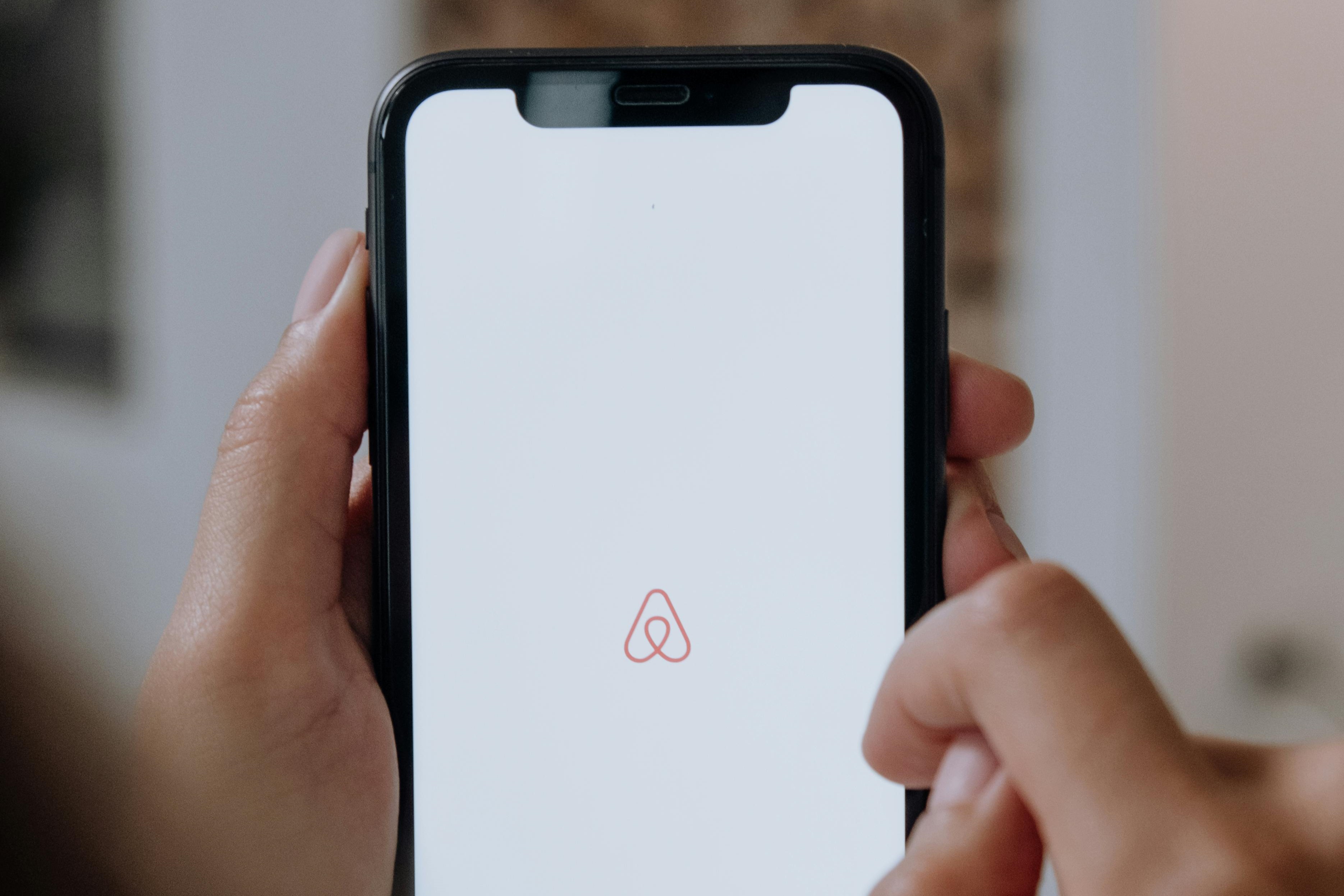 A phone shows the Airbnb logo