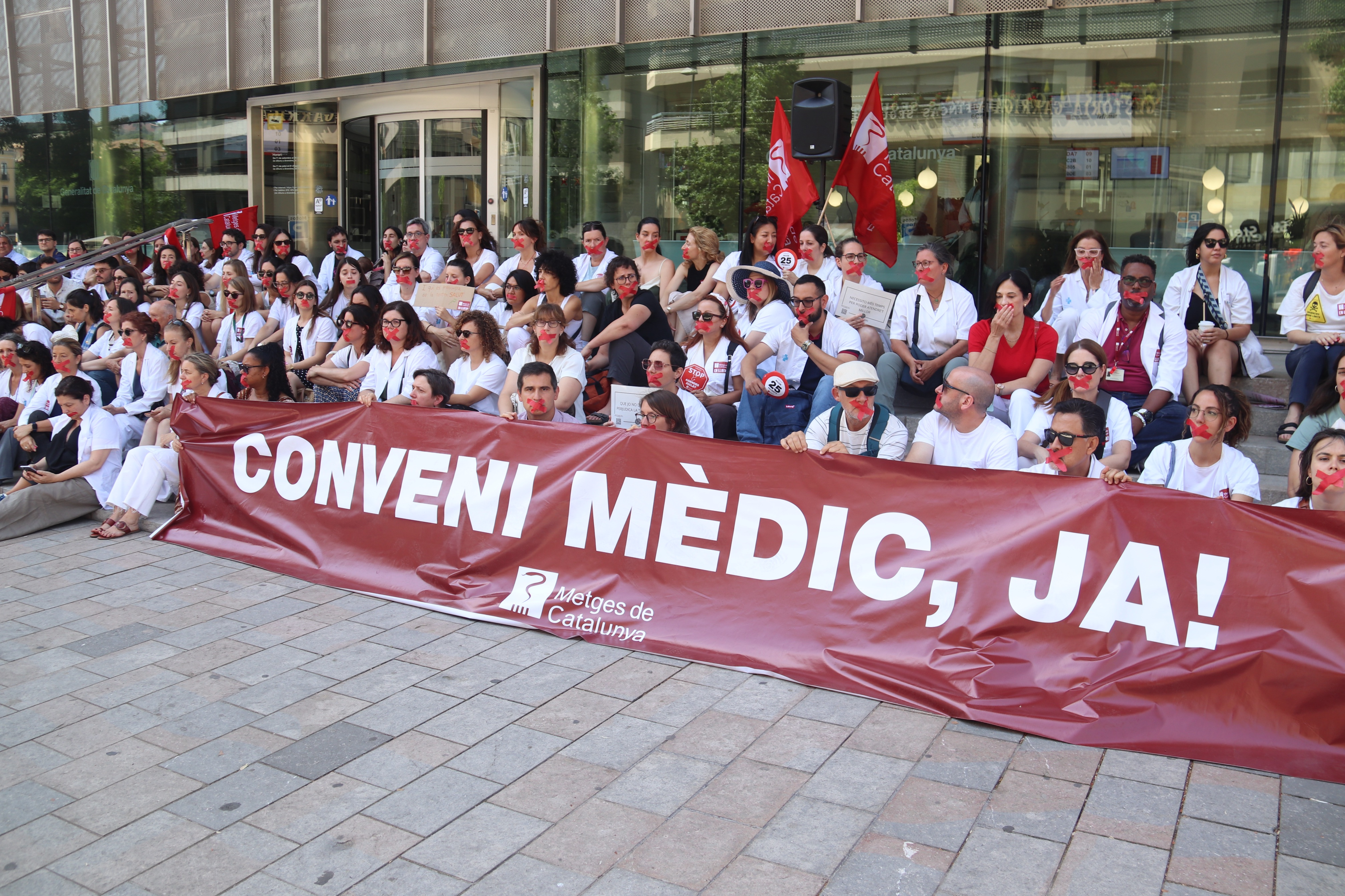 Around 100 doctors in Girona cover their mouths with red tape during a protest calling for a collective agreement