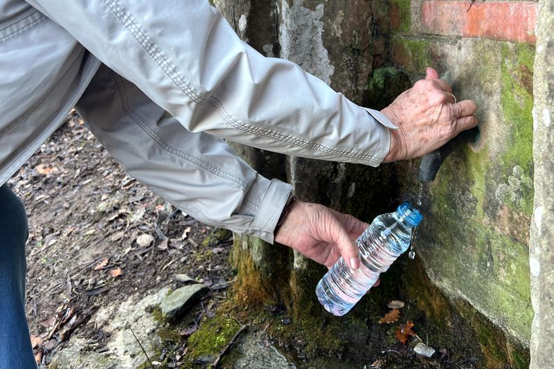 A person fills up a bottle of water in a fountain in Figueral, in Calldetenes