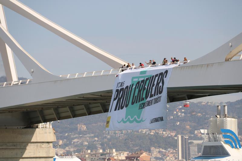 CUP members hanging a large poster against cruise ships from a bridge at the Barcelona port