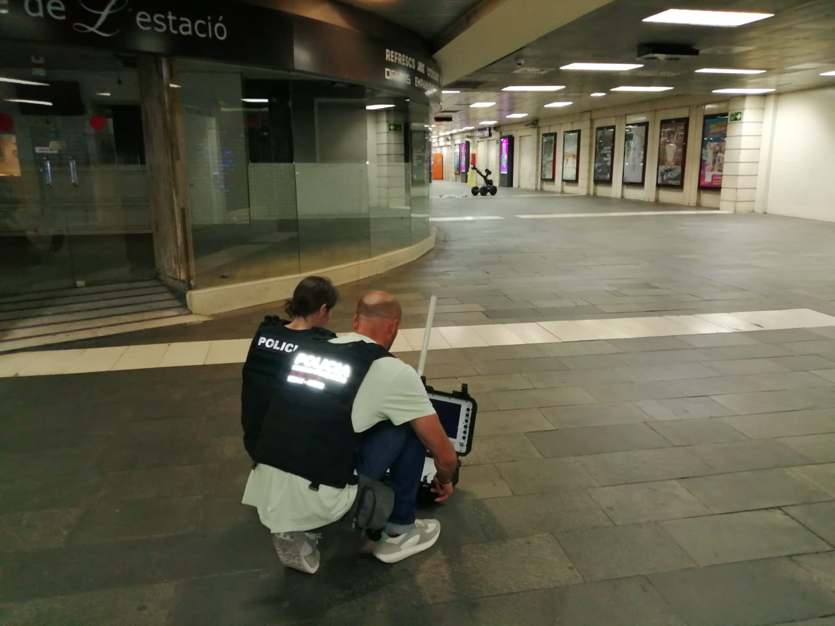 Two Catalan police officers guide a robot to look into the suspicious object in a bin at Barcelona's Plaça Catalunya, on June 27, 2023