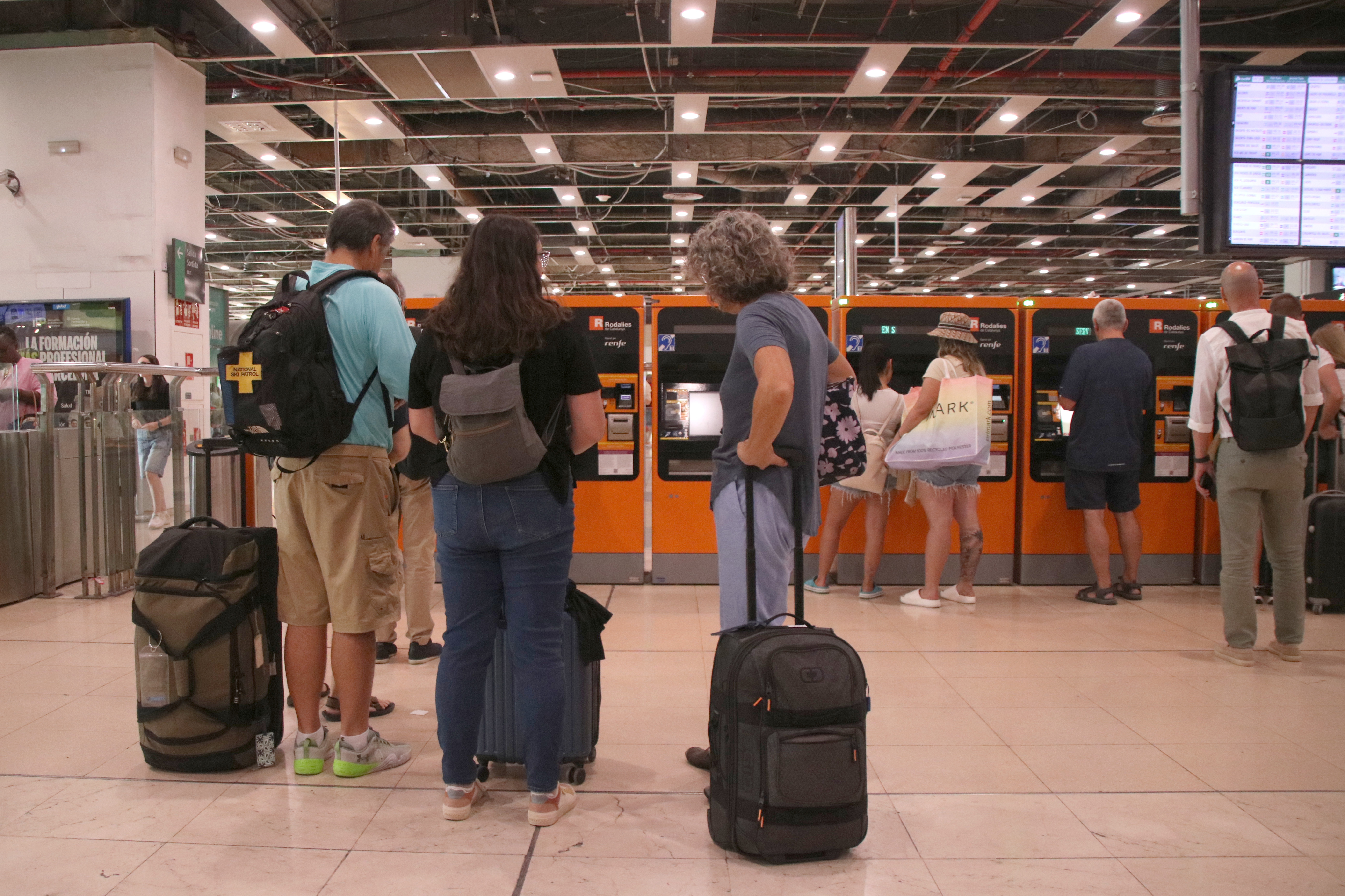Passengers queue to use a ticket machine at Sants station