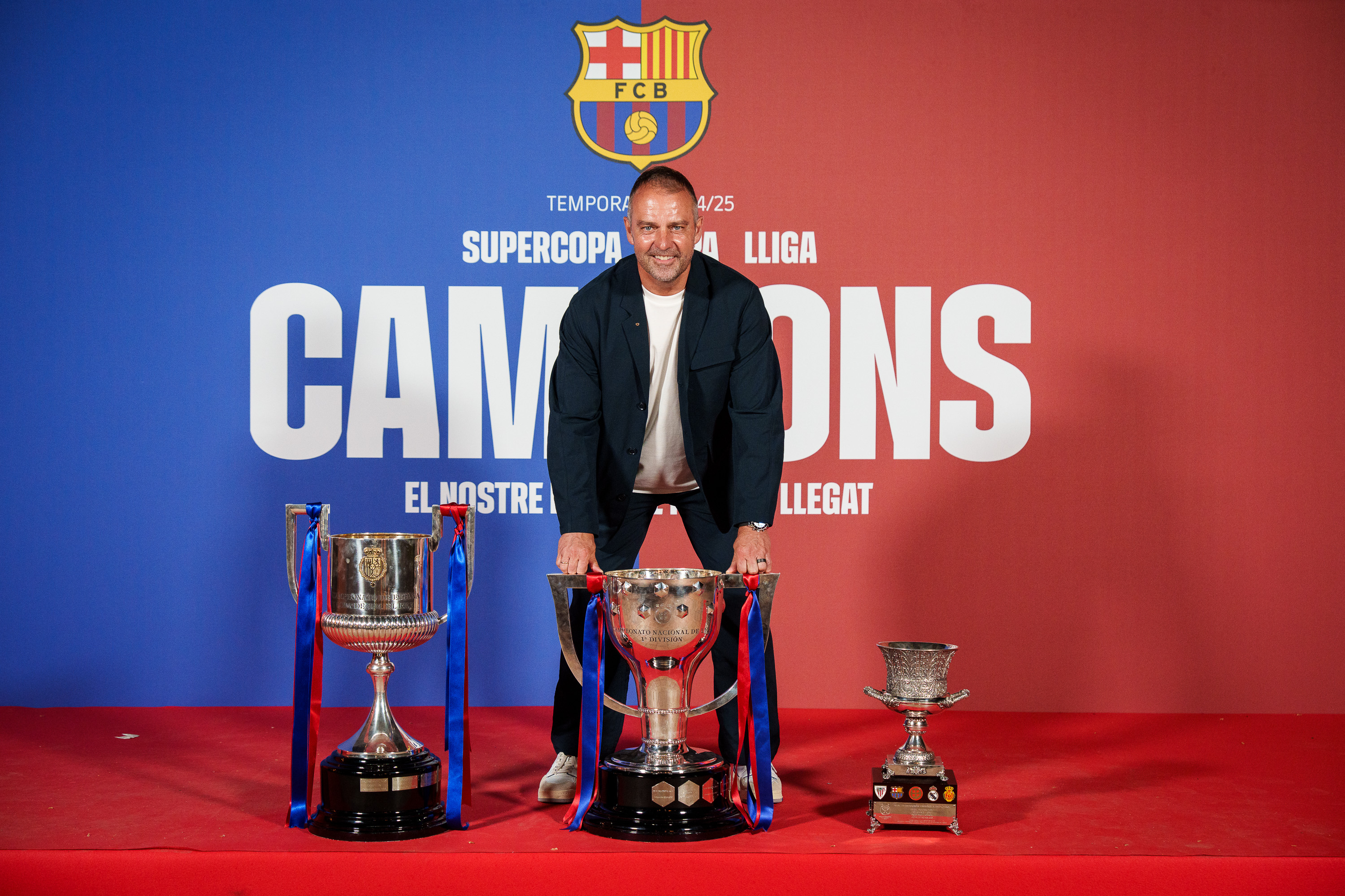 FC Barcelona head coach Hansi Flick poses with the 2024/25 La Liga, Spain's Super Cup, and the Spanish Copa del Rey trophies