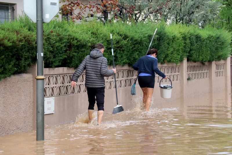 Two people walking with buckets in flooded streets in Tarragona