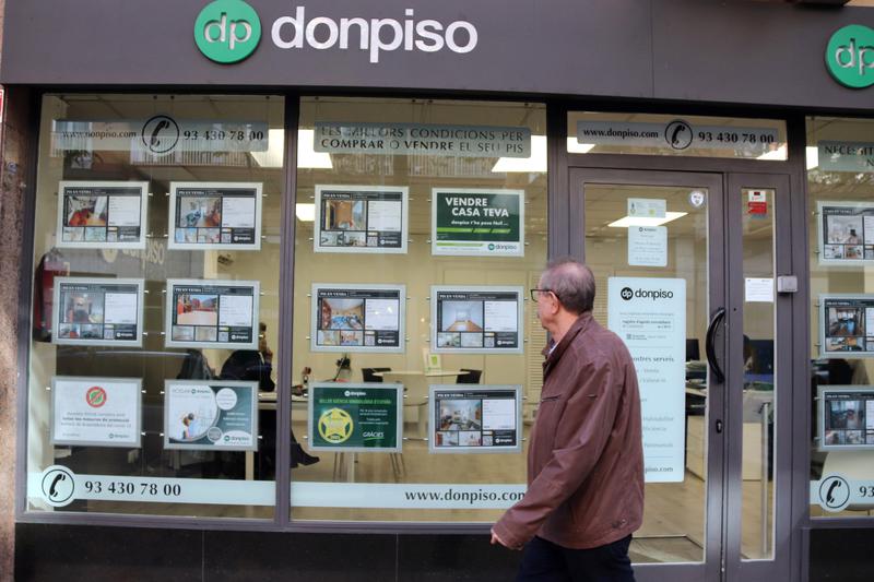 A person walks in front of a 'Donpiso' real estate agency where some flats and apartments are for sale and rent 