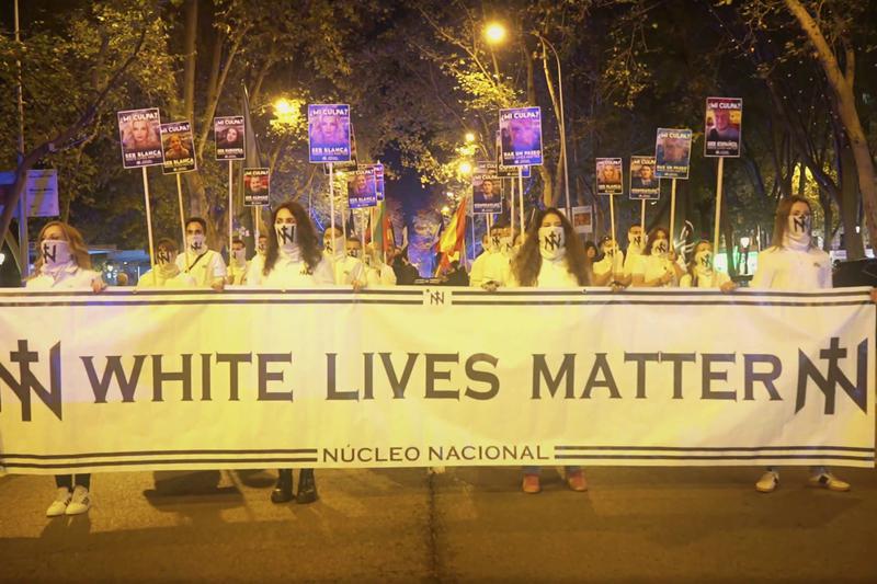 Núcleo Nacional members with their faces covered, holding a sign that reads "White Lives Matter"