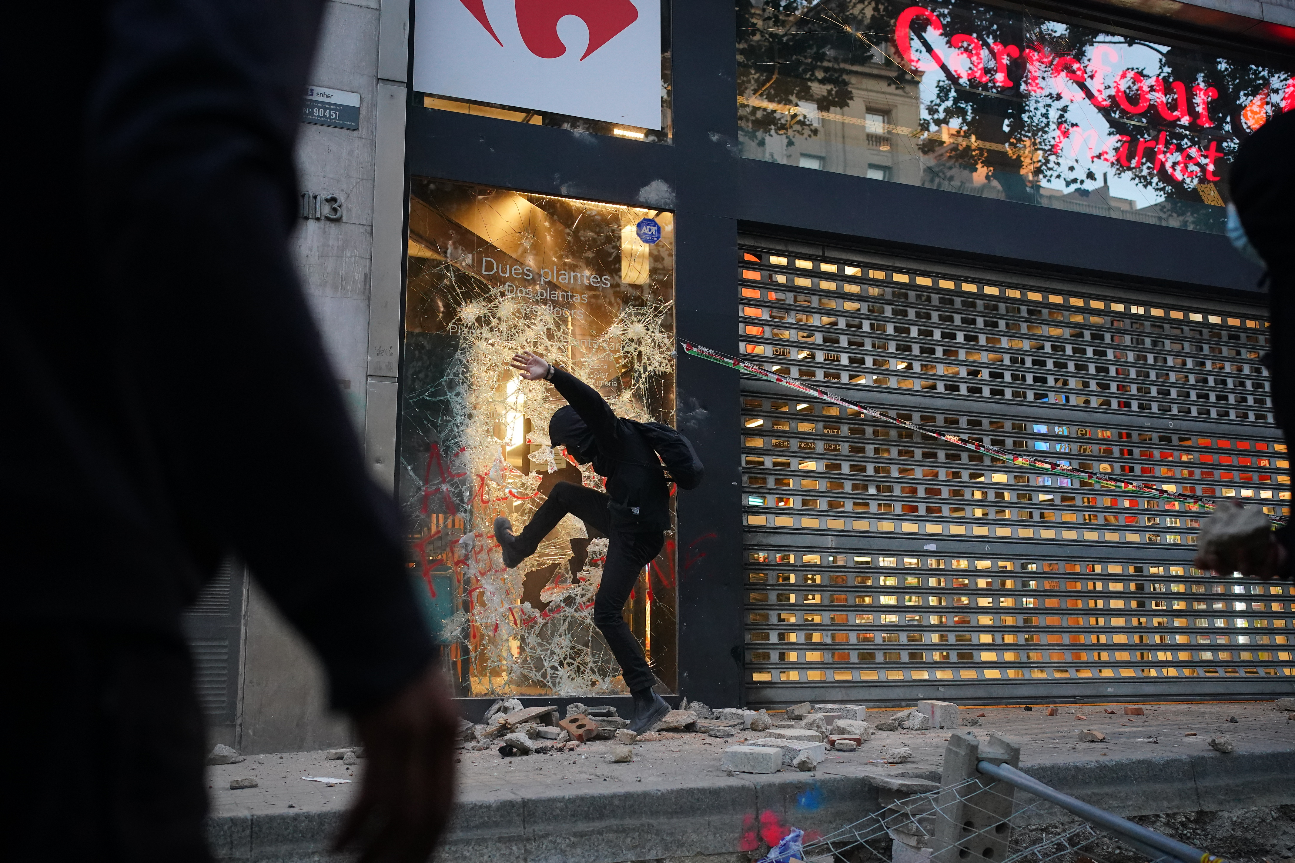 A hooded protester causes damage to a supermarket chain store on Barcelona's La Rambla