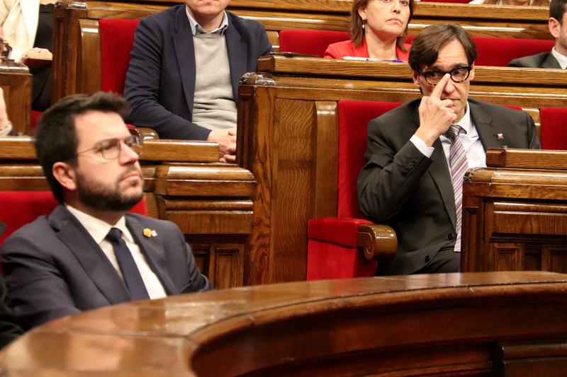 Socialist leader Salvador Illa on the right, touches his glasses, while Catalan president Pere Aragonès, on the left, stares at the parliament speaker out of frame on January 26, 2023